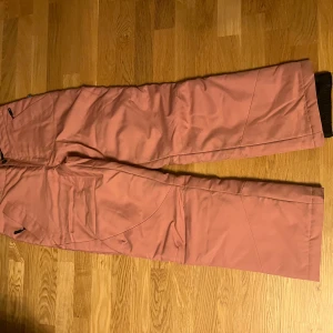 Rosa täckbyxor från Ski Industries S - Rosa täckbyxor från Ski Industries i storlek S. Byxorna är vind- och vattentäta med WR system 2000 och har raka ben, dragkedja och knapp framtill. Perfekta för vinterns alla äventyr i backen eller snön.