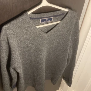 Grå stickad tröja Hansen & Jacob -  Grå stickad tröja från Hansen & Jacob med v-ringning och mörkblå förstärkningar på armbågarna. Tröjan har  en klassisk passform som funkar till allt. Perfekt för kyliga dagar. Ny pris:2000 mitt pris 500. Kom med bud