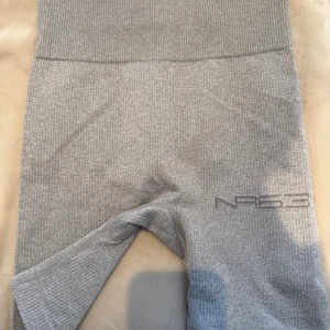 Grå ribbade shorts från New Apparel - Säljer ett par grå ribbade shorts från New Apparel. De är högmidjade och har en tight passform, perfekta för träning eller chill. Materialet är mjukt och stretchigt, och shortsen har en diskret logga på benet. Supersnygga och bekväma!