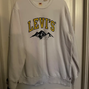 Vit sweatshirt från Levi's - Vit sweatshirt från Levi's med stort gult och svart tryck framtill och motiv av berg. Klassisk rund halsringning och långa ärmar.