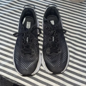 Svarta Hoka Rincon 3 sneakers - Säljer ett par Hoka Rincon 3 sneakers i svart med vita detaljer och vit sula. Perfekta för träning och löpning, med lätt och mjuk känsla. Hoka-logga på sidan och hälen. Använda 3 gånger därav lite smutsiga, annars finns det inga skavanker på skorna! Storlek 37 1/3                                        Nypris: 1500