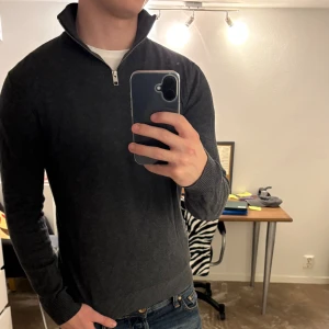 Mörkgrå halvzip tröja i ullblandning - Snygg mörkgrå långärmad tröja från Jack & Jones med halv dragkedja vid kragen. Tröjan är i mjuk ullblandning. Perfekt för lager-på-lager och chill stil. Tröjan är i xs men passar nästan mig (186cm) tack vare de stretchiga materialet. Mått finns på bilderna men som sagt passar den både större och mindre tack vare stretchen. Vid frågor hör av dig! 