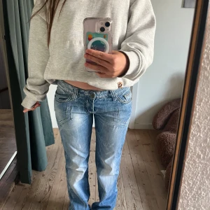 Blåa jeansbyxor från Chip & Bakk - Säljer ett par blåa jeansbyxor från Chip & Bakk med snygga slitningar och kontrastsömmar. Byxorna har låg midja, raka ben och coola detaljer på bakfickorna med broderi. Perfekta för dig som gillar en avslappnad och trendig look.