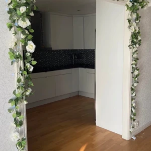 Ljusslinga med vita rosor - Dekorativ ljusslinga med vita konstrosor och gröna blad. Slingan har små blå LED-lampor som ger ett mysigt sken, perfekt för att rama in dörröppningar eller väggar. Fint skick, inga synliga defekter eller slitage. Skapar en romantisk och inbjudande atmosfär i hemmet.man kan köpa ljusslinga till om man vill.