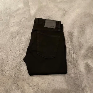 Svarta slim fit jeans från s.Oliver - Svarta jeans från s.Oliver, modell Keith Slim Fit. Snyggt smal passform med klassisk femficksdesign och bälteshällor. Jeansen är tillverkade i denim och har en stilren look som funkar till många olika outfits. Perfekt för dig som gillar en modern och enkel stil.