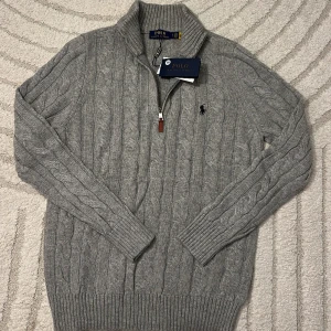 Grå kabelstickad tröja Polo Ralph Lauren - 🩶 Polo Ralph Lauren stickad tröja Helt ny och aldrig använd, med alla taggar kvar! Tyvärr för liten för mig, så säljer den vidare. Klassisk grå kabelstickad design med halv dragkedja och ikoniska Polo-loggan 🐎  💸 Pris: 699 kr ✨ Perfekt för dig som vill ha en tidlös och snygg tröja i toppskick!