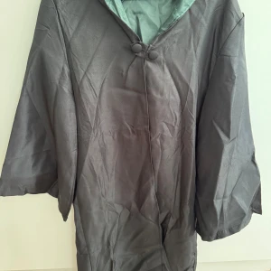 Harry Potter-utklädnad med tillbehör - Slytherin-utklädnad bestående av en lång kappa, glasögon, trollstav, slips och en halsduk   Storlek S  Endast kappan har öppnats ur förpackningen, utklädnaden har aldrig använts 