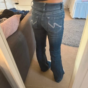 Blå bootcut jeans med broderade fickor - Snygga blå jeans med bootcut-modell och broderade detaljer på bakfickorna. Jeansen har klassisk femficksdesign, normal passform och är tillverkade i jeansmaterial. Perfekta för dig som gillar en retrovibe och vill ha ett par jeans som sticker ut lite extra. Pris kan diskuteras vid snabb affär 