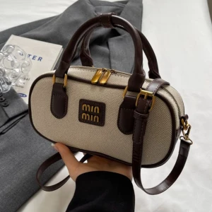 Beige handväska från Min Min - Snygg beige handväska från Min Min med svarta eller mörkbruna detaljer och guldfärgade metalldragkedjor. Väskan har oval form, dubbla handtag och justerbar axelrem. Materialet är canvas med detaljer i skinnimitation. Perfekt för dig som vill ha en stilren och trendig accessoar.