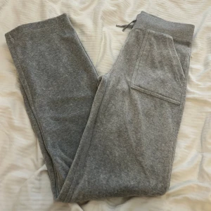 Gråa mjukisbyxor Juicy Couture - Gråa Del Ray mjukisbyxor från Juicy Couture i modellen Track Pant Silver Marl. Byxorna har bred resår i midjan med snörning, stora fickor fram och bakfickor med knappar. Mjukt material och relaxed fit med raka ben.