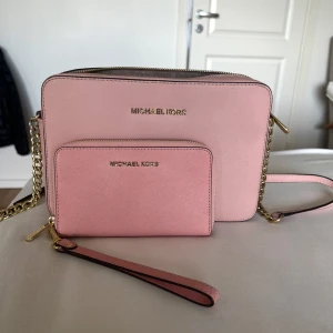 Rosa axelväska och plånbok Michael Kors - Snygg ljusrosa axelväska från Michael Kors med matchande plånbok. Väskan har guldfärgade detaljer, kedjerem och dragkedja. 
