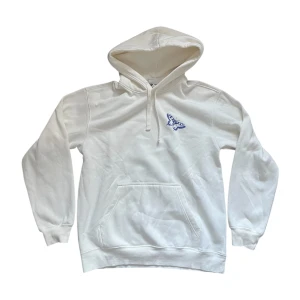 Vit hoodie - Vit hoodie med blå fjärilstryck på bröstet och stort blått texttryck på ryggen. Klassisk känguruficka, dragsko i huvan och mjukt material. Perfekt för dig som gillar stilrena plagg med en twist.