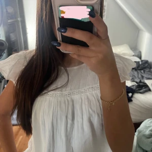 Vit somrig blus med spetsdetalj - Säljer en vit blus med romantiska volangärmar och fin spetsdetalj vid bröstet. Den har en luftig passform och är perfekt för varma dagar. Materialet känns lätt och mjukt mot huden, och den har en söt, feminin look.