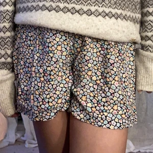 Blommiga shorts från Kappahl  - Säljer ett par färgglada shorts från Kappahl med blommigt mönster i pastellfärger som rosa, blå, gul och lila. De har elastisk midja och är gjorda i ett lätt och mjukt material som känns skönt mot huden. Perfekta för varma dagar och chill outfits.