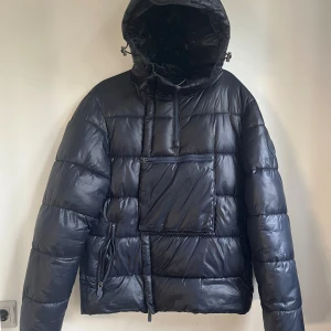 Midnattsblå pufferjacka Michael Kors - Säljer en midnattsblå pufferjacka från Michael Kors med huva och stora fickor med dragkedja. Jackan har ett stilrent MK-märke på ärmen och quiltad design. Perfekt för kalla dagar med sin tjocka och fluffiga look. Dragkedja framtill och justerbar huva. Använd en vinter med inga defekter. Storleken upplevs större