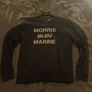 Blå sweatshirt från Morris - Säljer en marinblå sweatshirt från Morris med vit text 'MORRIS BLEU MARINE' på bröstet. Tröjan har rund hals, långa ärmar och ribbade muddar. Skön och stilren. Materialet är mjuk bomull. SKRIV VID MINSTA FRÅGA, PRIS KAN DISKUTERAS.