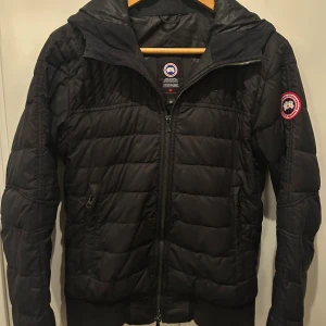 Svart Cardigan Canada goose  - Hej! Säljer nu en svart Canada Goose Cabri Hoddy med huva och klassisk logga på ärmen. Skick 7/10. Storlek S. bara använd ett fåtal gånger. Priset kan såklart alltid att diskuteras. Hör av er vid frågor!