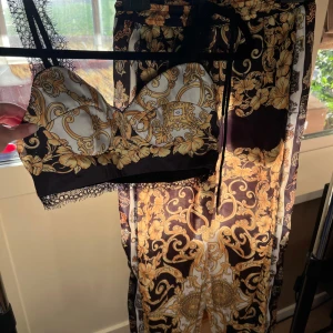 Svart och guldig topp med byxor - Säljer ett vackert set från Bella Barnett. Tyget är som siden och väldigt vackert. Använt bara ett par gånger, tyvärr har det blivit för litet för mig :(