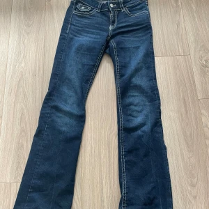 Mörkblå bootcut jeans med kontrastsömmar - Snygga mörkblå jeans med bootcut passform och tydliga vita kontrastsömmar. Klassisk femficksmodell med lock på bakfickorna och silverfärgade knappar. Jeansen har låg midja och är tillverkade i stretchigt denim för en bekväm känsla. Från Gina tricot young 
