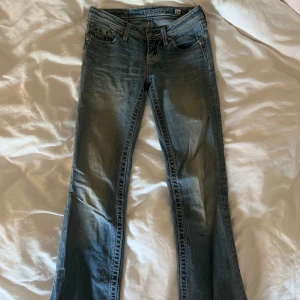 Miss Me ljusblå bootcut jeans med detaljer - Snygga ljusblå jeans från Miss Me med bootcut passform. Jeansen har broderade bakfickor med nitar, kedjor och dekorativa knappar. Klassisk femficksmodell med låg midja. Två knappar saknas och lite slitna ner till men ingen man tänker på. Skriva privat för fler bilder.