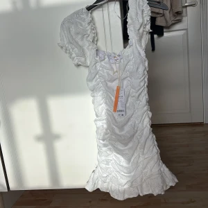 Vit kort klänning med volangärm - Superfin vit kort klänning från Gina Tricot Young med puffiga volangärmar och broderade detaljer. Klänningen har rynkade partier och söt spetsstruktur som ger en romantisk vibe. Perfekt för sommarens alla tillfällen!
