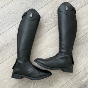 Svarta ridstövlar från CRW, stl 39 - Säljer mina ridstövlar då de är för stora för mig. De är använda några fåtal gånger men ett veck framtill där hästen trampade på skon (syns på bild) annars i fint skick. De är väldigt bekväma och lätta att hålla rena. Org pris: 799kr, pris kan diskuteras.
