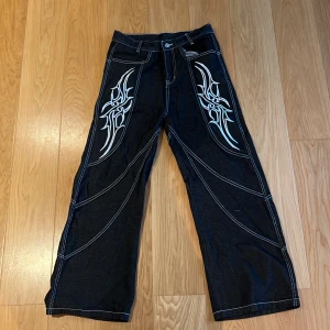 Svarta wide jeans med tribal mönster - Säljer ett par svarta jeans med bred passform, tribal mönster och vita kontrastsömmar. Fick detta jeanspar i present och har endast använts en gång men väljer att sälja då den inte passade.