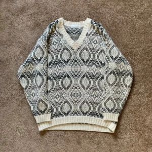 Mönstrad stickad tröja Marks & Spencer - Stickad tröja från Marks & Spencer med snyggt geometriskt mönster i beige, grått och svart. V-ringad med ribbade muddar och avslut. Materialmix av akryl, alpacka och ull gör den både mjuk och varm. Perfekt för kyliga dagar.