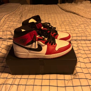 Nike Air Jordan 1 Chicago sneakers - Säljer ett par Nike Air Jordan 1 Chicago sneakers med klassisk färgblockning i rött, vitt och svart. Skorna har högt skaft, svart snörning och rund tå. Ovandelen är i skinn med perforering på tån och den röda yttersulan ger extra attityd. Perfekt för dig som vill sticka ut. Storlek 44, skorna är använda en skoldag, och har bara stått på hyllan sen dess, vill bli av med, priset är ej hugget i sten! Original karton medföljer!