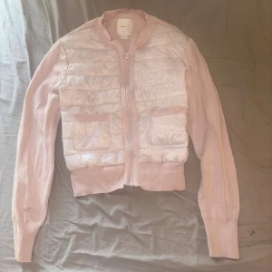 Ljusrosa cardigan jacka från Gina Tricot - Säljer en ljusrosa cardigan jacka från Gina Tricot med quiltad, glansig front och stickade ärmar. Jackan har två fickor framtill och dragkedja hela vägen upp. Perfekt för dig som gillar en chill och snygg look. Passar st XS. Använd typ 2-3 gånger