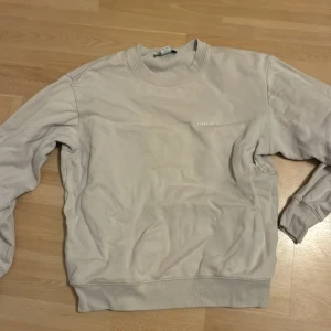 Beige sweatshirt från Tiger of Sweden - Säljer en stilren beige sweatshirt från Tiger of Sweden med diskret logga på bröstet. Tröjan har rund hals, ribbade muddar och är långärmad. Perfekt för en clean och avslappnad look.