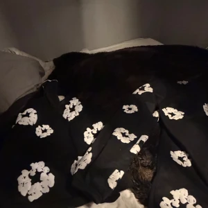  Denim Tears set  - Svarta mjukisbyxor från Denim Tears med stora vita blommönster över hela byxorna. Byxorna har en avslappnad passform och är gjorda i mjukt bomullsmaterial. Perfekt för chill dagar och streetwear-stil.