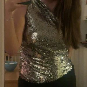 Glitter topp oneshoulder - Säljer en glittrig silvrig topp med paljetter och oneshoulder-design. Toppen är tight och har en snygg asymmetrisk axel som ger en cool och festlig vibe. Säljer då den inte kommer till användning längre. Vid fler bilder, hör av er💕