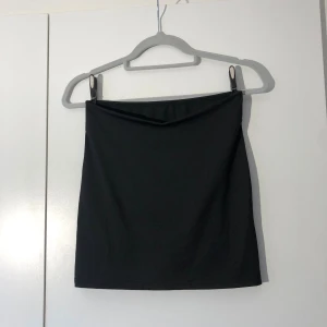 Svart tight kortkjol i polyester - Stretchig kjol med en v formning i fram. Midjemått ca 65cm. Längd ca 40cm. Pris: 10kr 