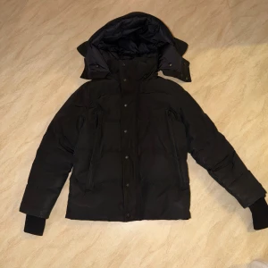 Canada gosse jacka - Denna svarta Canada Goose-jacka är använd men i gott skick. Den har kvar sin form och funktion, med endast mindre tecken på normalt slitage. En varm och slitstark jacka som fortfarande fungerar utmärkt för kalla vinterdagar.