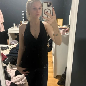 Svart omlott halterneck linne - Säljer ett svart halterneck linne med omlott-skärning och djup v-ringning. Toppen är ärmlös och har en stilren, tight passform som framhäver axlarna. Perfekt för dig som gillar en enkel men snygg look.