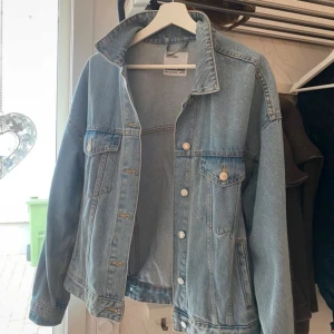 Ljusblå jeansjacka från Bershka - Säljer en klassisk ljusblå jeansjacka från Bershka i storlek M. Jackan har en oversized passform, knappar framtill och två bröstfickor med lock. 
