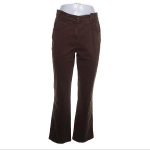 Bruna bootcut byxor från Ulfin - Snygga bruna bootcut-byxor från Ulfin med klassisk femficksdesign och knappstängning. Byxorna har en högre midja och är tillverkade i bomull med lite stretch för extra komfort. Perfekt för dig som gillar retrovibbar och vill ha en cool siluett.