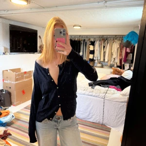 Mörkblå kofta med stjärndetalj - Mysig mörkblå kofta med knappar framtill och lång ärm. På ena ärmen finns en cool silverfärgad stjärna som detalj. Koftan har en avslappnad passform och är stickad i ett mjukt material. Perfekt att slänga över en t-shirt eller linne.