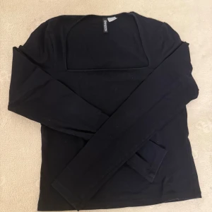 Svart topp  - En svart långärmad topp från H&M Divided med fyrkantig ringning. Enkel och stilren design i mjuk bomull, perfekt att matcha med jeans eller kjol. Snygg passform och klassisk look som funkar året runt.