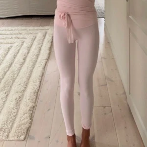 Ljusrosa leggings med knyt i midjan - Supersnygga ljusrosa leggings med hög midja och knytband. Stretchigt material som sitter tight och följer kroppen perfekt. Perfekta för dans, yoga eller chill hemma. Enkel design utan mönster, ger en clean och fräsch look. Lululemon inspererade 