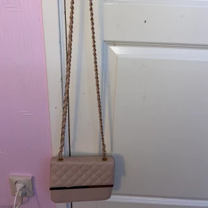 Fin rosa och guldig liten väska! - En rosa och guldig liten väska som är lätt att ta med t.ex när man ska åka iväg och shoppa. Även perfekt att förvara saker i. Använd men i fint skick. Inuti har den en liten ficka med dragkedja. 