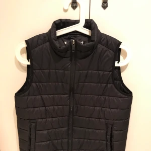 Svart Everest väst  - Säljer min fina väst från Stadium i st 146/152, men kan passa ungefär vem som helst. Den är i helt nyskick och säljer för 150kr eller högsta bud 🤗 köparen står för frakten🥰