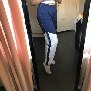 Nike byxor strl. M - Ett par nike byxor i strl. M. Byxorna är använd endast en gång och är i nyskick. Röda knappar efter utsida benen som går att knäppa upp och snöre i midjan. Hör av dig vid frågor eller fler bilder! 220kr kr eller högsta bud om fler är intresserade!✨