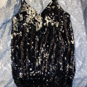 Klänning - En glittrande svart paljett klänning. Oanvänd.Prislapp sitter kvar. Går till knäna i längden. 