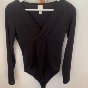 Svart långärmad body - En svart långärmad body med v-ringning köpt på hm i glansigt material. Väldigt fin men kommer inte till användning 