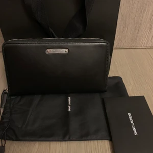 Saint Laurent Pouch/Lång Plånbok - Helt ny Sant Laurent Pouch/Long Wallet. Väldigt många kortfack (se bild) och även 2 större fack varav en med dragkedja. Som sagt helt ny, kommer med tags dustbags och kvitto från Saint Laurent butik. Pris i butik 4800kr. Kan sälja med SafePay if så önskas