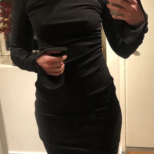 Tajt, ribbad klänning  - Mycket fin ribbad klänning med draperidetaljer vid ärmarna och längst ena sidan vilket gör att den blir ”sne” längst ner. Slits på ärmarna och en snett skuren hals. 