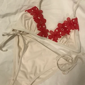 Broderad bikini - Världens finaste krämvita bikini med röda broderade blommor🥰🥰 säljer då överdelen tyvärr blivit för liten, passar 65-70 A😇 Underdelen knyts i i sidan och har lite rysch baktill☺️ skickar inte bilder hur den sitter på privat❣️ frakt kostar 33kr☺️