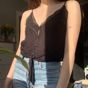 H&M topp storlek 34 - säljer denna gulliga topp från h&m! den är typ knappt använd så i väldigt gott skick. det är ett svart tunt tyg med upphöjda små prickar, knappar längs mitten och spetsdetaljer i ringningen. axelbanden är justerbara. 100% viskos. passar xs-s🖤